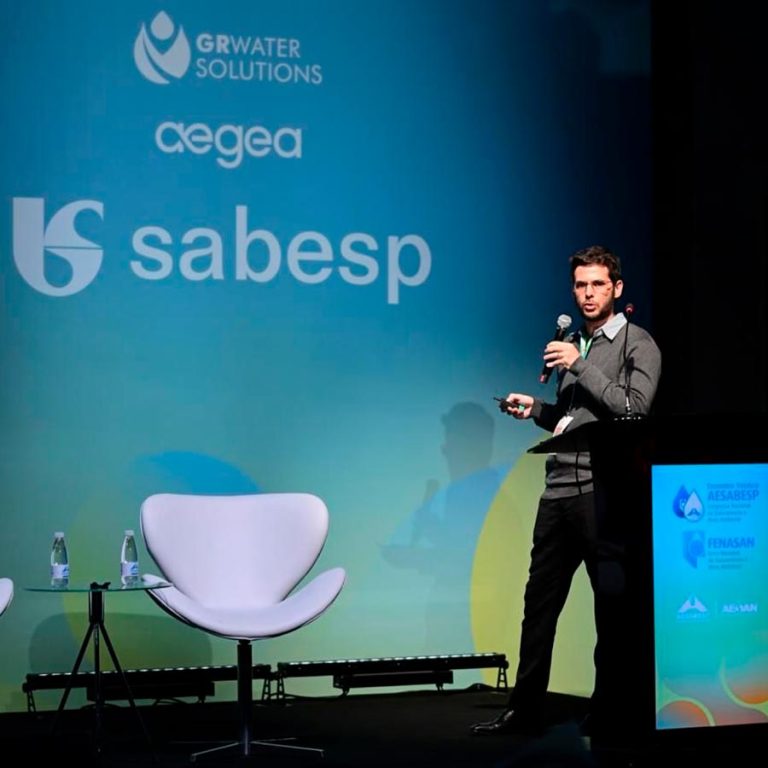 Consultor da Kurita apresenta soluções de gestão hídrica no palco do Encontro Técnico AESabesp e Fenasan, com painel da Sabesp e Aegea ao fundo.